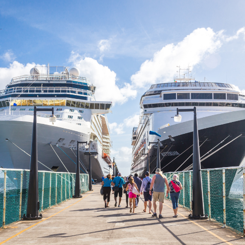 Tourists walking on a sunny pier between two large cruise ships